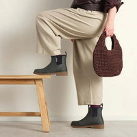 Behind The Trees - Person wearing beige pants and black boots, holding a brown woven bag. - Merry People - Bobbi Ankle Boot - Charcoal