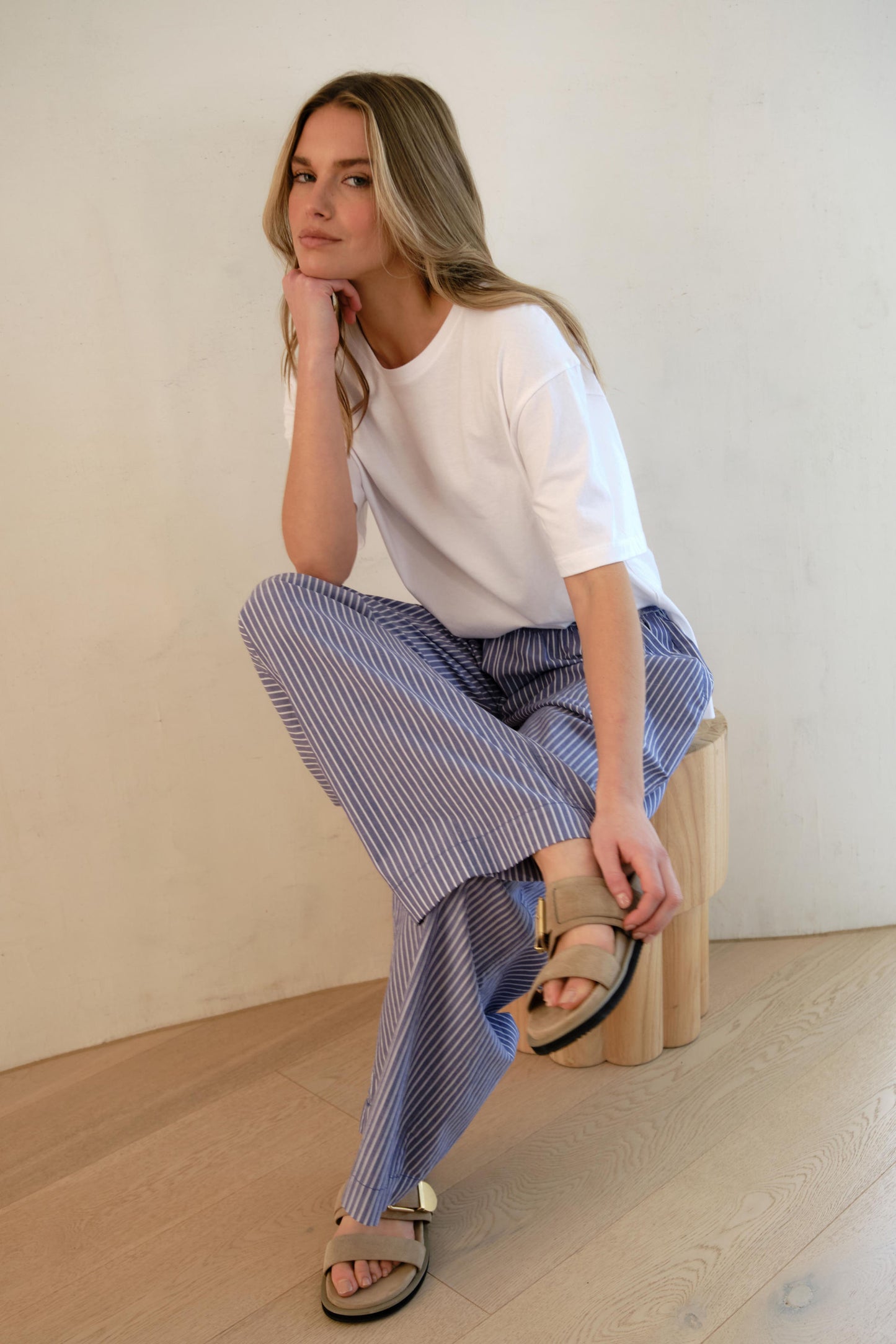 Behind The Trees - Woman wearing a white t-shirt and blue striped pants standing against a plain wall. - Ceres Life - Stevie Slouchy Tee - White