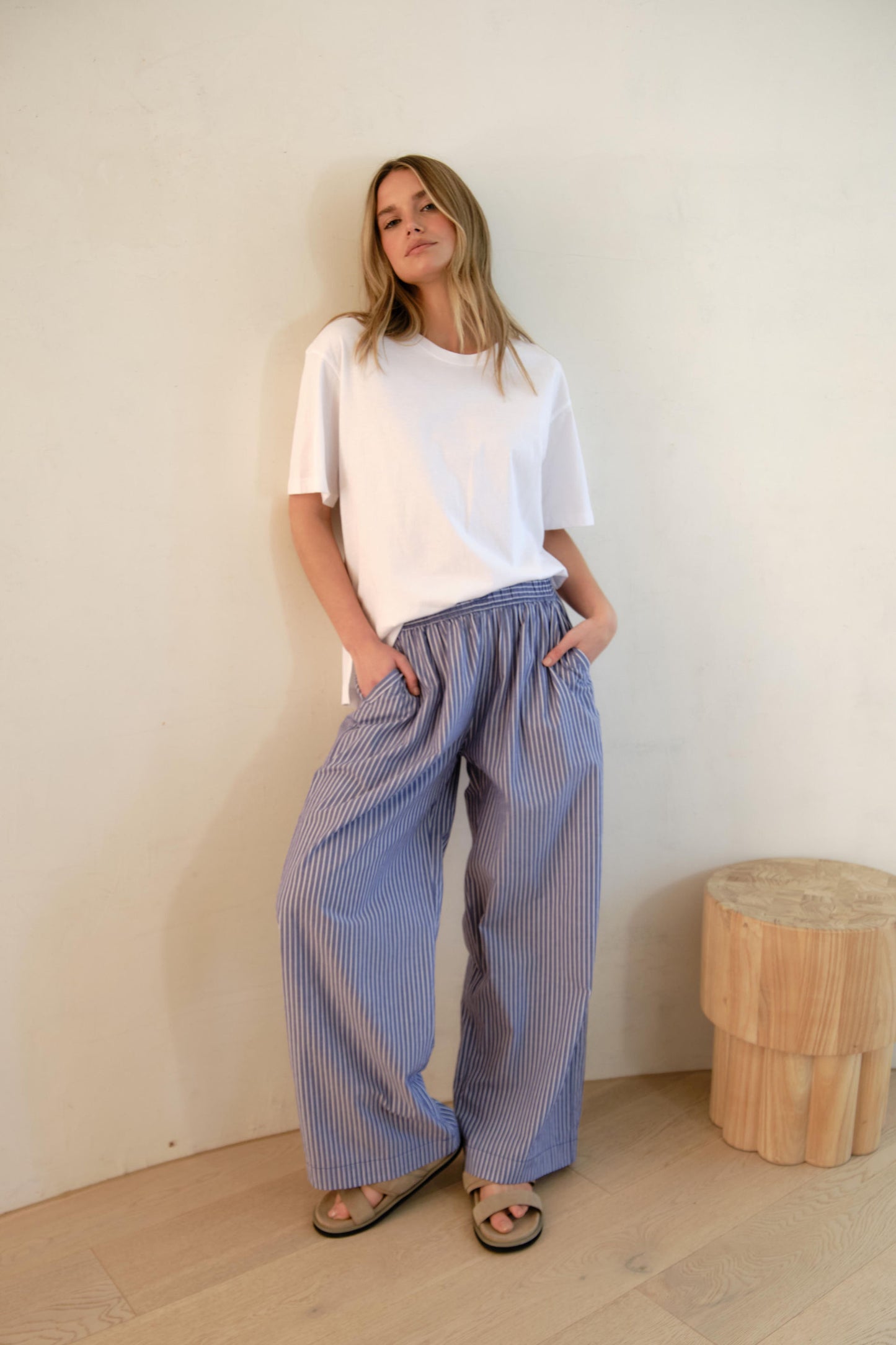 Behind The Trees - Woman wearing a white t-shirt and blue striped pants standing against a plain wall. - Ceres Life - Stevie Slouchy Tee - White