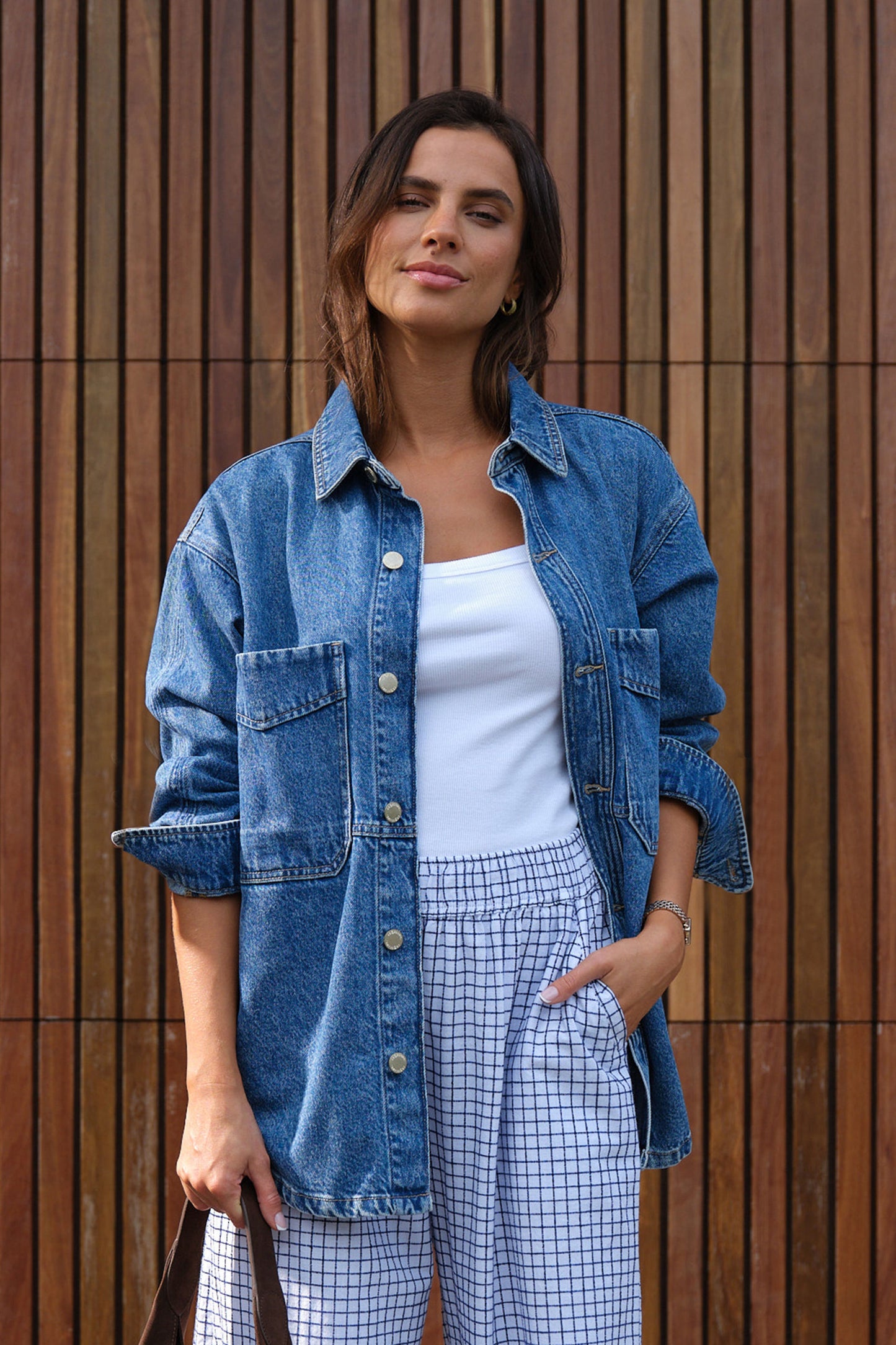 Behind The Trees - Woman wearing a denim jacket and checkered pants standing against a wooden wall. - Ceres Life - Bobbi Side Pocket Denim Shacket - Indigo