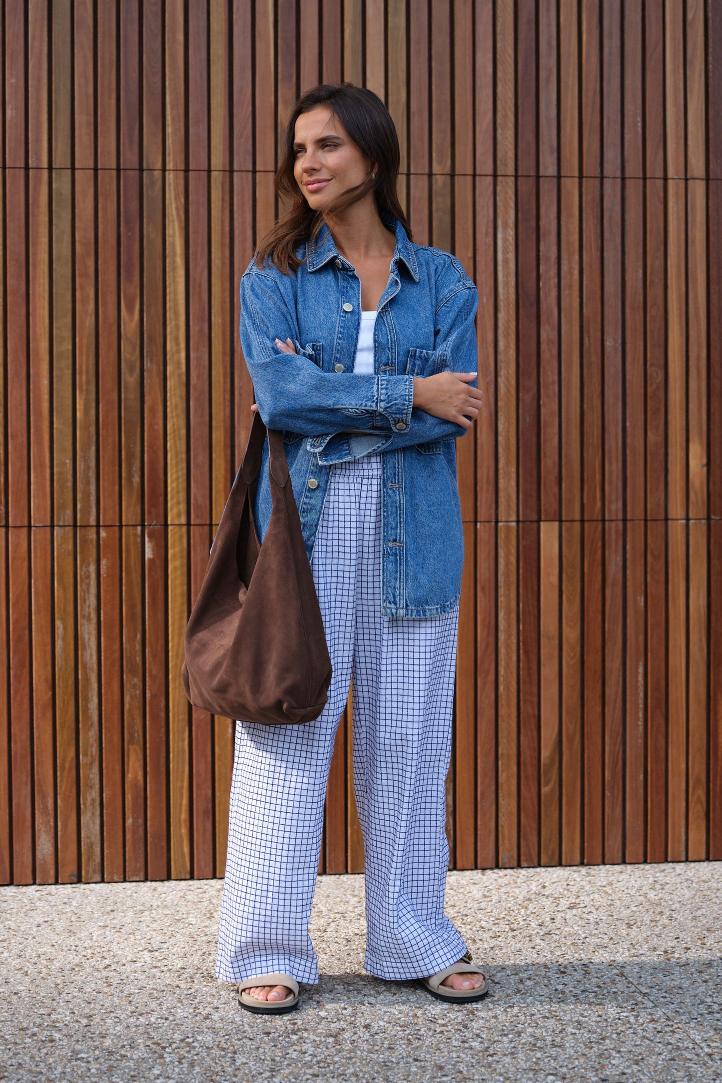 Behind The Trees - Woman wearing a denim jacket and checkered pants standing against a wooden wall. - Ceres Life - Bobbi Side Pocket Denim Shacket - Indigo