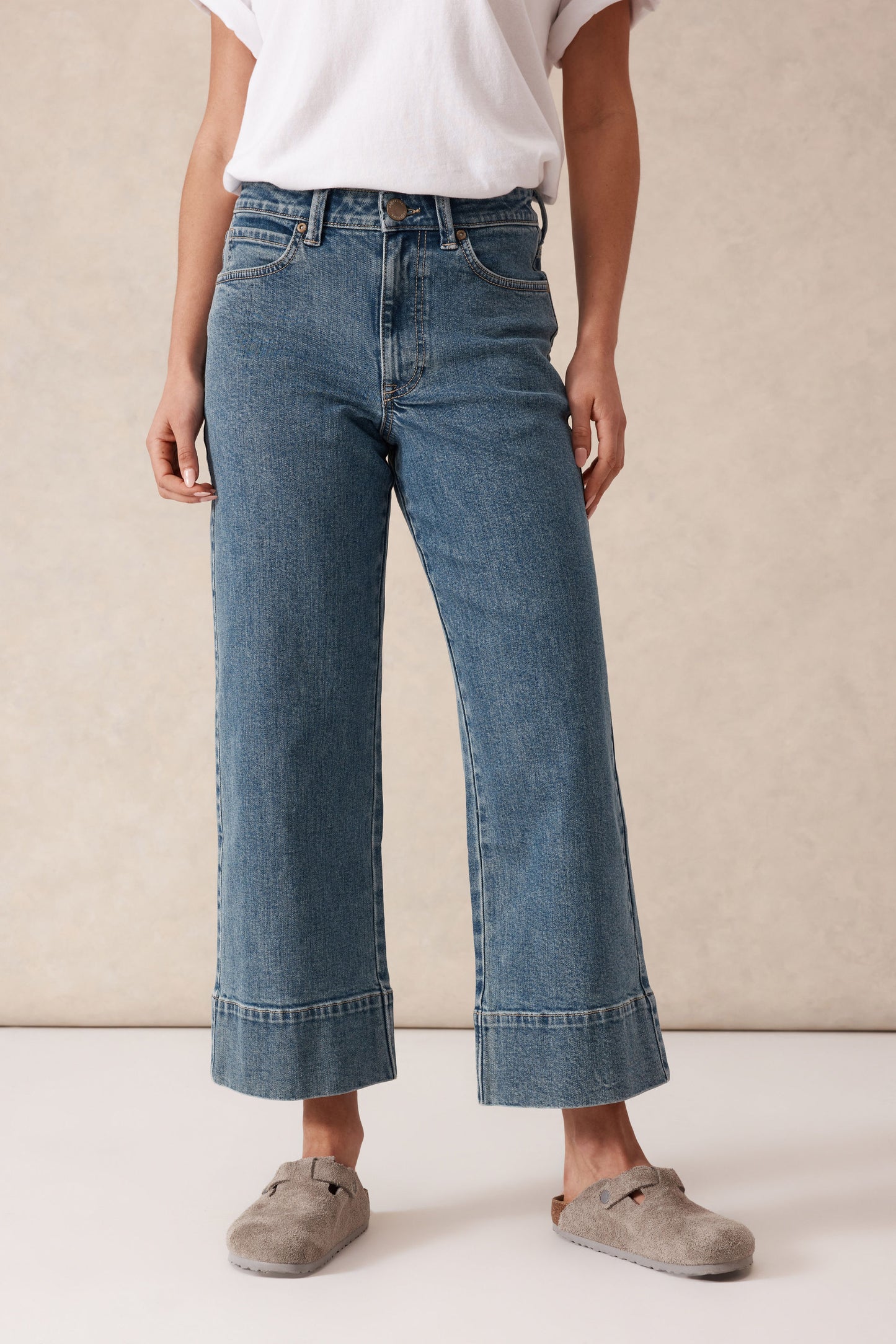 Behind The Trees - Woman wearing a white t-shirt with text and blue jeans against a beige background - Ceres Life - Jude Wide Leg Crop Jean - Mid Indigo