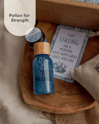Behind The Trees - Blue bottle labeled 'Spirit of Atlantis' on a wooden surface with a tag reading 'I am Strong'. - The Little Potion Co - Mini Potion Kit - Moonlight Waters