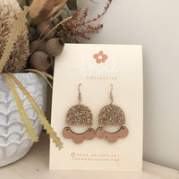 Behind The Trees - Gold earrings on a card with 'Foxie Collective' branding, placed on a surface with decorative elements. - Foxie Collective - Marlie Earrings - Gold Glitter & Cherry Wood