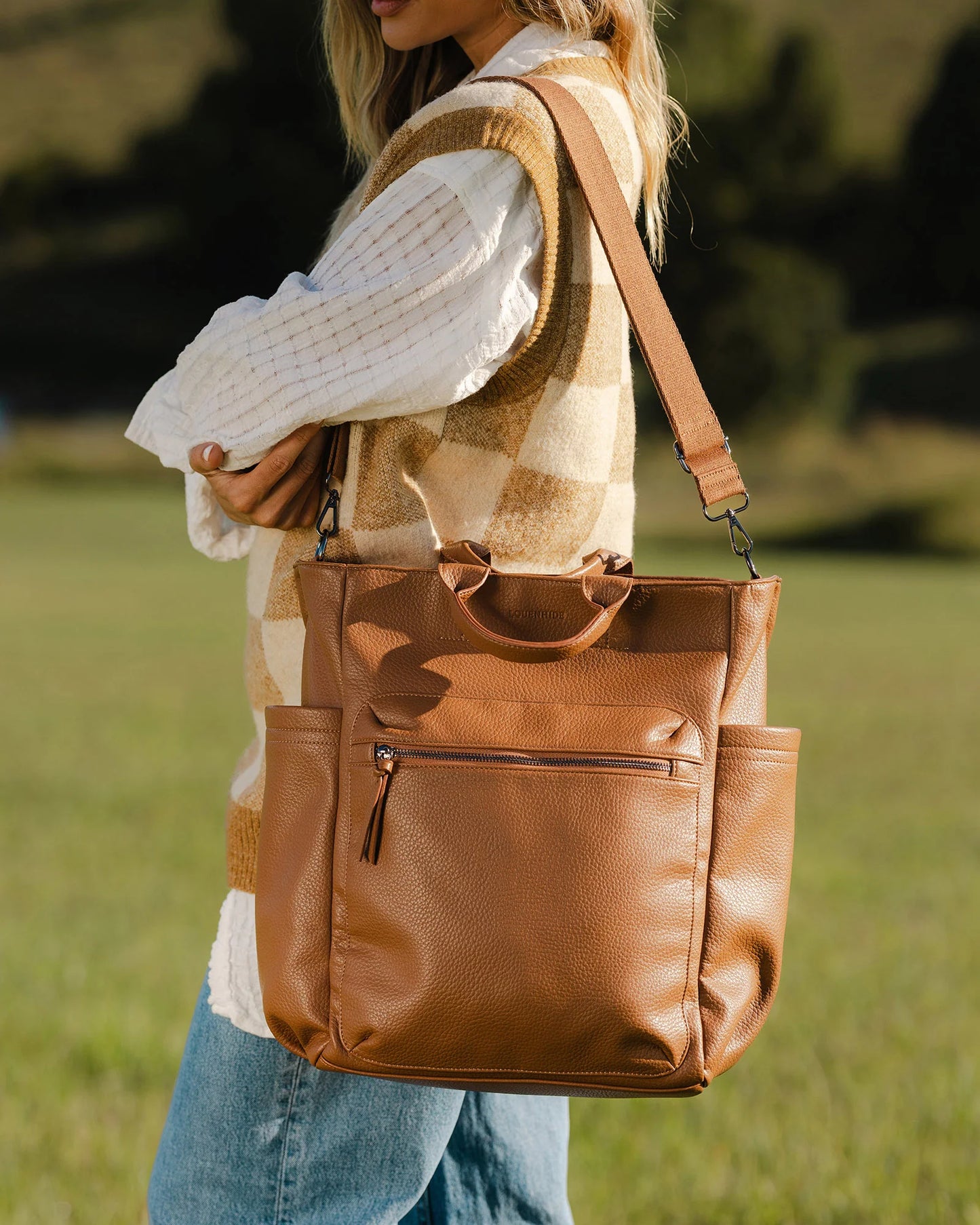 Behind The Trees - Person holding a brown leather backpack in a grassy field - Louenhide - Bronx Backpack - Nutmeg
