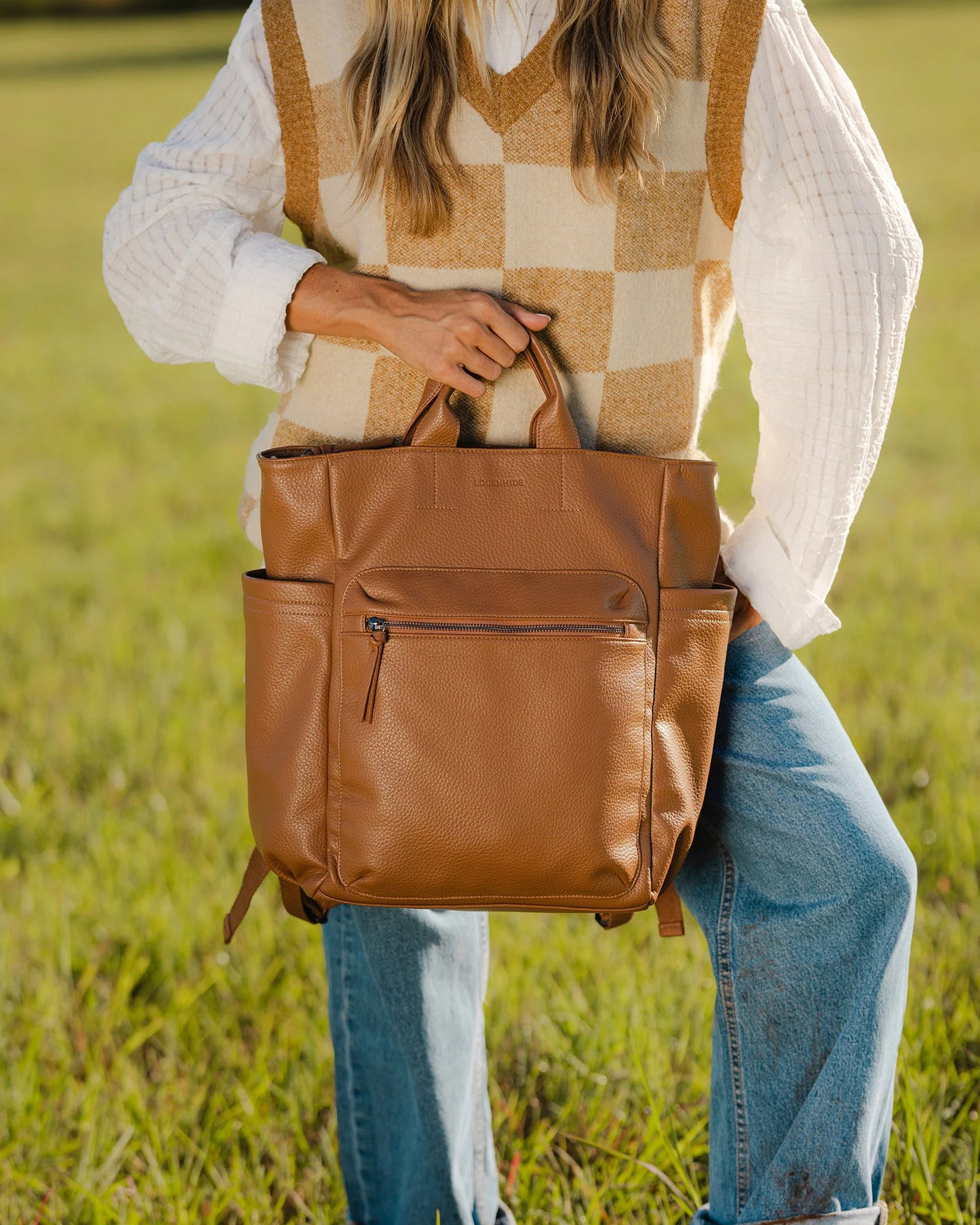 Behind The Trees - Person holding a brown leather backpack in a grassy field - Louenhide - Bronx Backpack - Nutmeg
