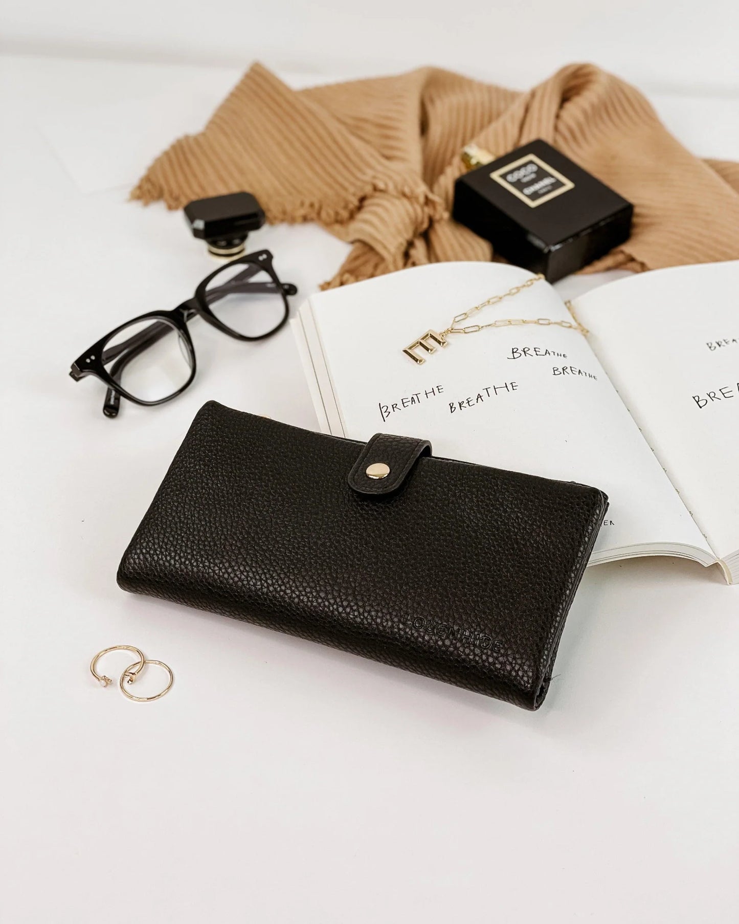 Behind The Trees - Black leather wallet on a white surface with glasses, perfume bottle, and open book. - Louenhide - Stella Wallet - Black