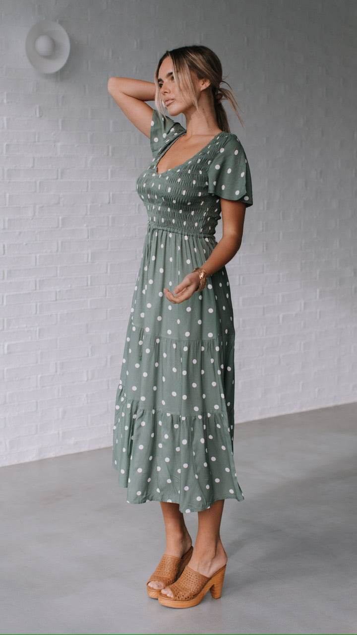 Behind The Trees - Woman wearing a green polka dot dress against a gray brick wall. - Grace & Co - Polka Dot Midi Dress - Khaki/White