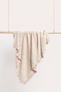 Behind The Trees - Beige textured blanket draped over a wooden rod against a white background - DLUX - Mica Chevron Pointelle Knit Baby Blanket - Shell