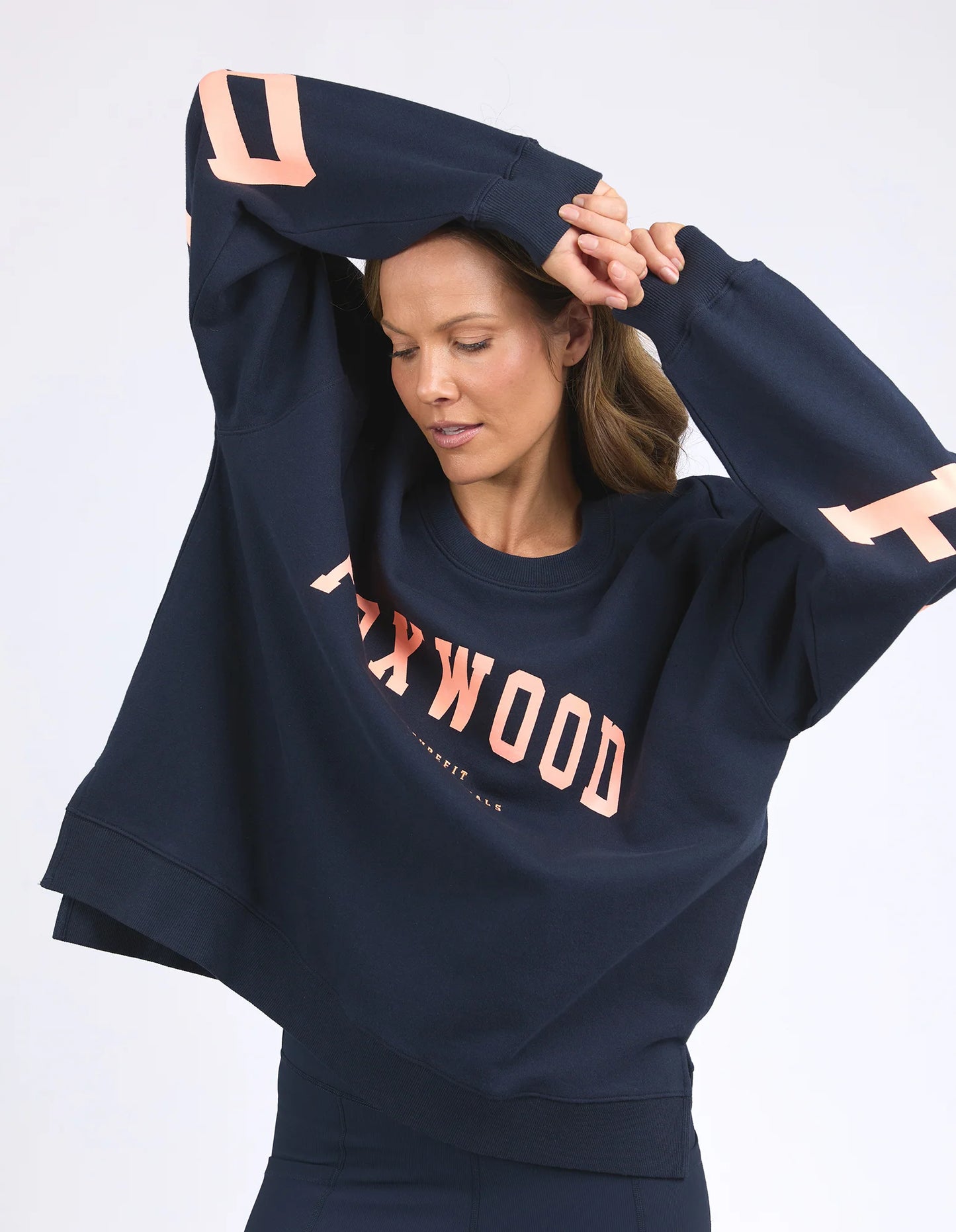 Behind The Trees - Woman wearing a navy blue sweatshirt with 'FOXWOOD' branding on a white background - Foxwood - Interval Crew - Navy with Peach