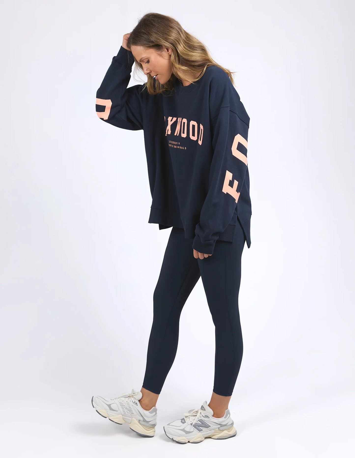Behind The Trees - Woman wearing a navy blue sweatshirt with 'FOXWOOD' branding on a white background - Foxwood - Interval Crew - Navy with Peach