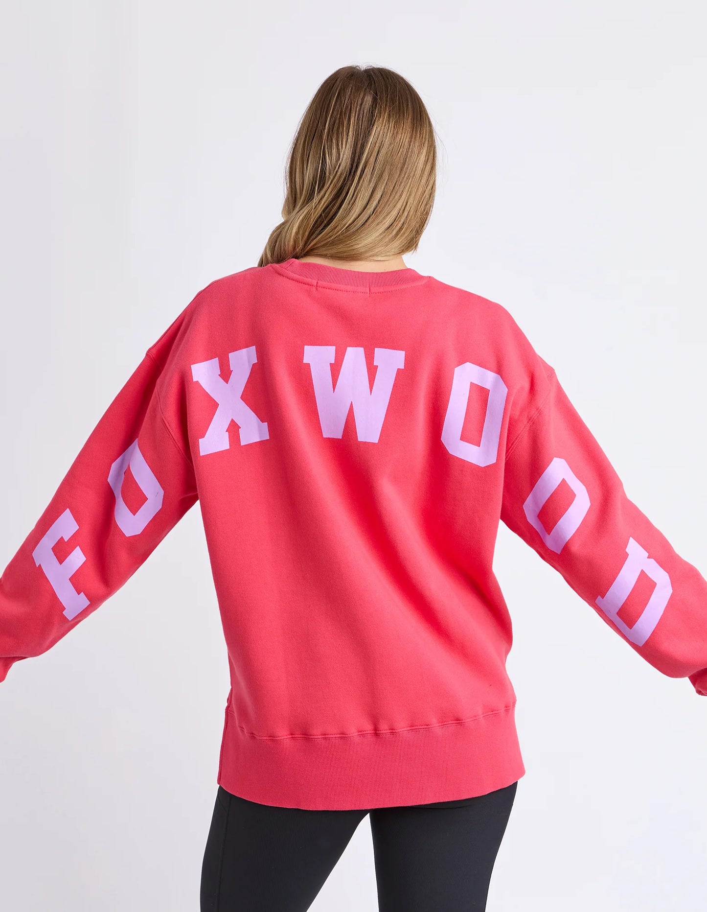 Behind The Trees - Woman wearing a red sweatshirt with 'Rockwood' text on a white background - Foxwood - Interval Crew - Raspberry & Neon Lilac