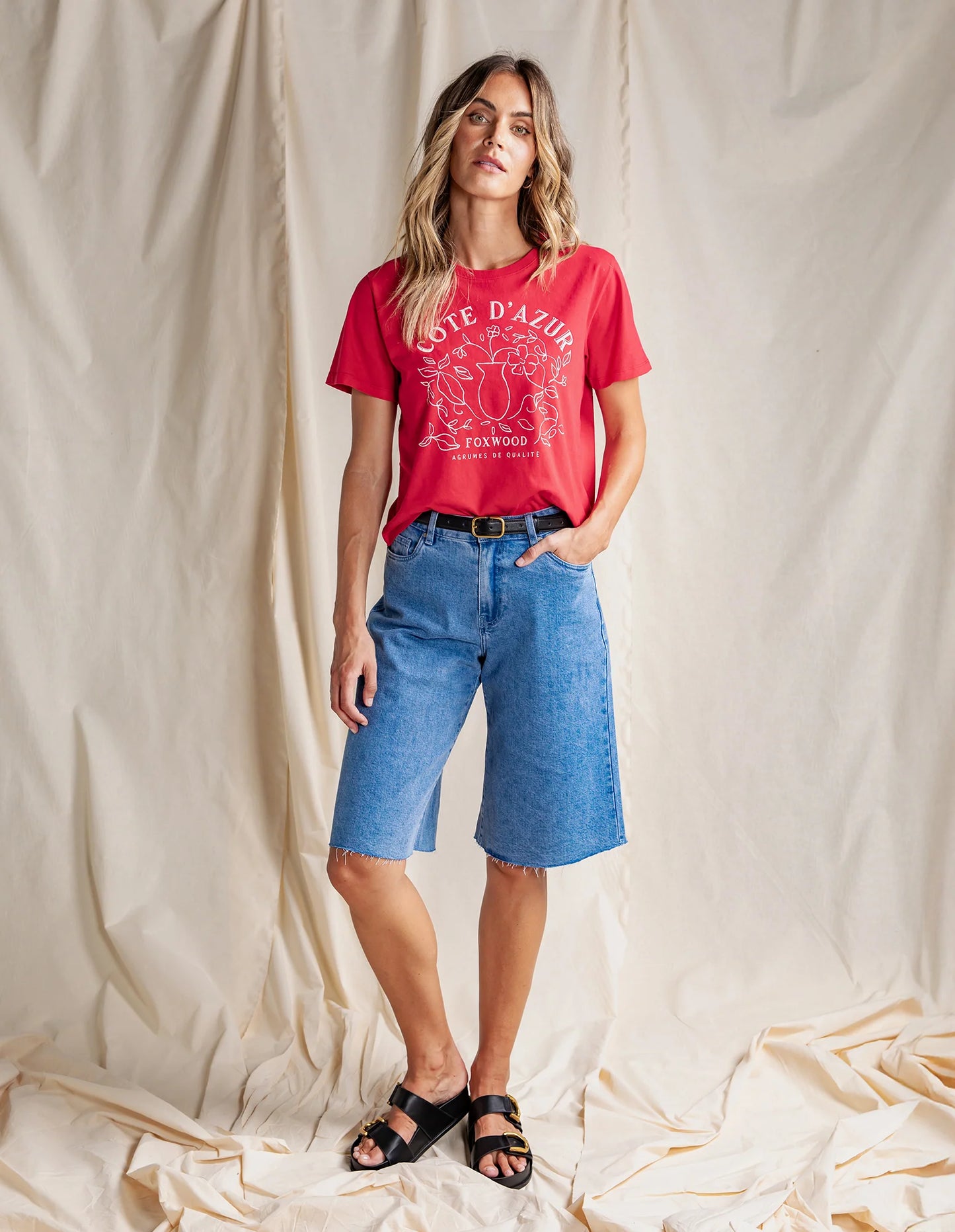 Behind The Trees - Woman wearing a red t-shirt with 'Cote d'Azur' design and white shorts on a light gray background