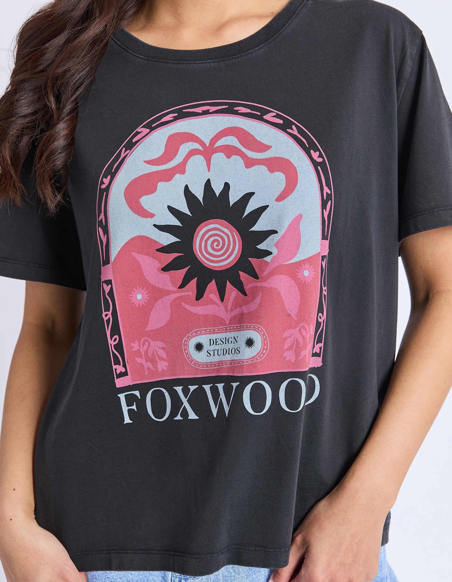 Behind The Trees - Woman wearing a black t-shirt with a graphic design and denim shorts on a white background - Foxwood - Nonchaliant Tee - Washed Black