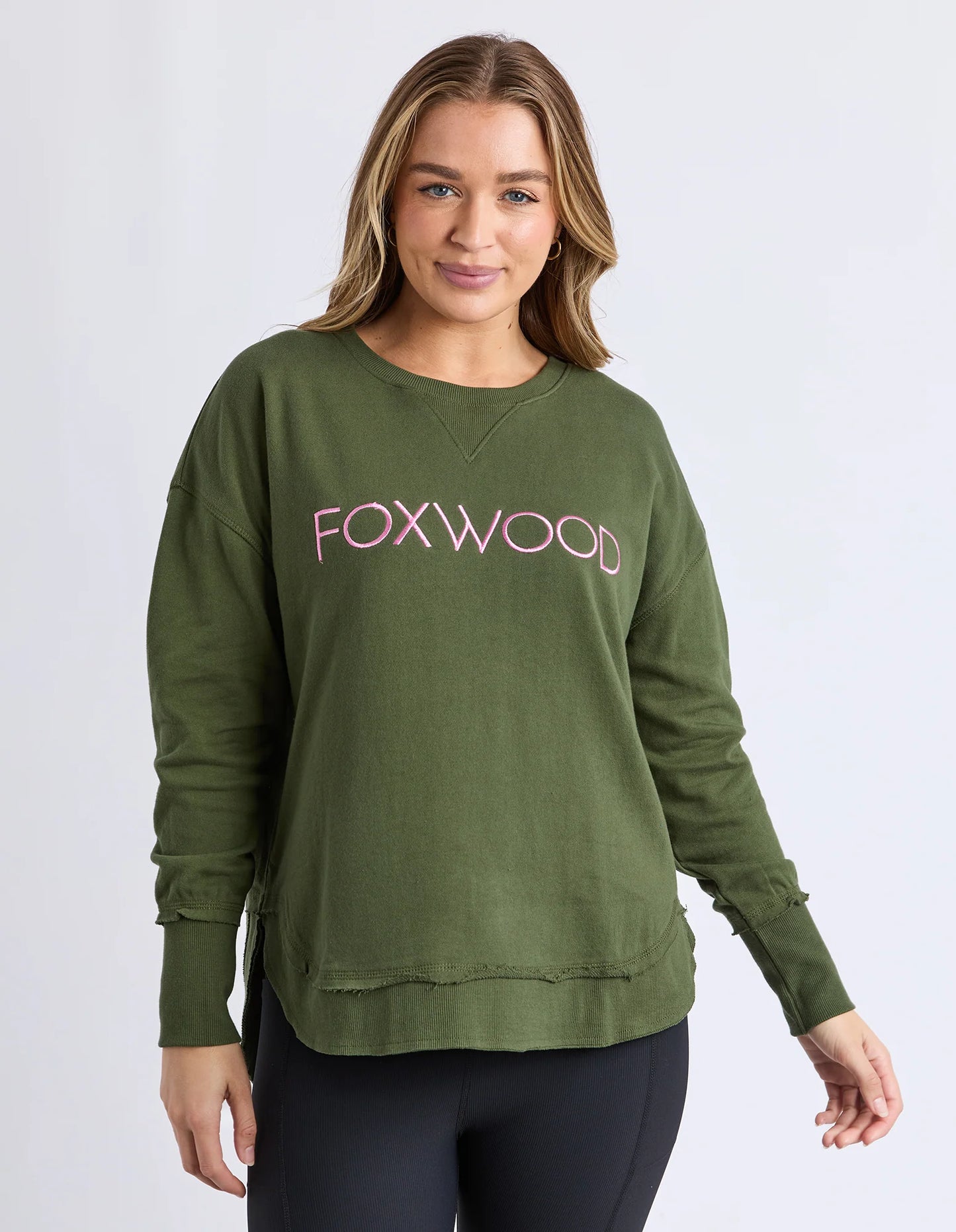 Behind The Trees - Woman wearing a green sweatshirt with 'FOXWOOD' text on a white background - Foxwood - Simplified Metallic Crew - Olive With Pink