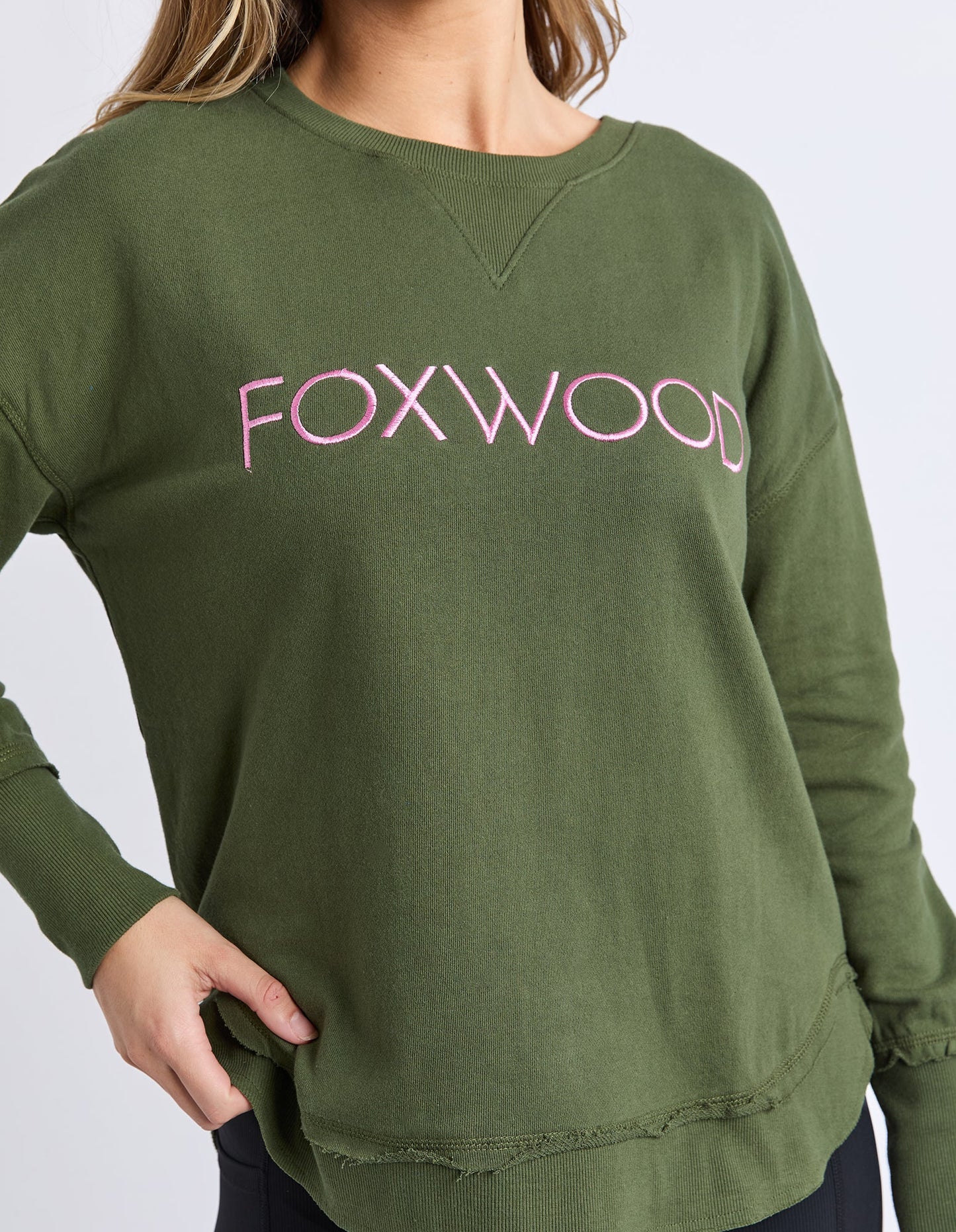 Behind The Trees - Woman wearing a green sweatshirt with 'FOXWOOD' text on a white background - Foxwood - Simplified Metallic Crew - Olive With Pink