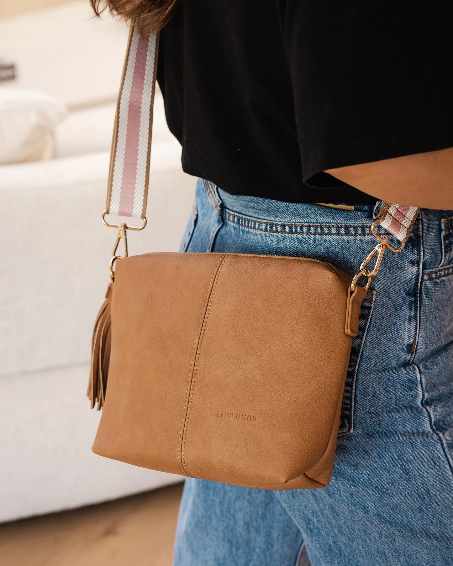 Behind The Trees - Woman holding a brown leather handbag with a pink strap in an indoor setting. - Louenhide - Kasey Crossbody Bag - Camel