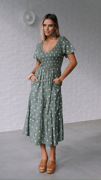 Behind The Trees - Woman wearing a green polka dot dress against a gray brick wall. - Grace & Co - Polka Dot Midi Dress - Khaki/White