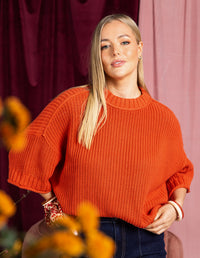 Behind The Trees - Woman wearing an orange sweater and blue jeans on a plain background - Elm - Luela Short Sleeve Knit - Orange