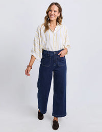 Behind The Trees - Woman wearing a white blouse with yellow stripes and blue jeans on a light gray background - Elm - Alyssa Front Pocket Jean - Sapphire
