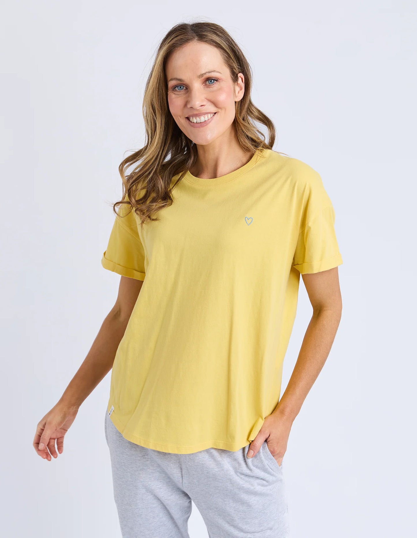 Behind The Trees - Woman wearing a yellow t-shirt with a small logo on a white background - Elm - Halli S/S Tee - Lemon