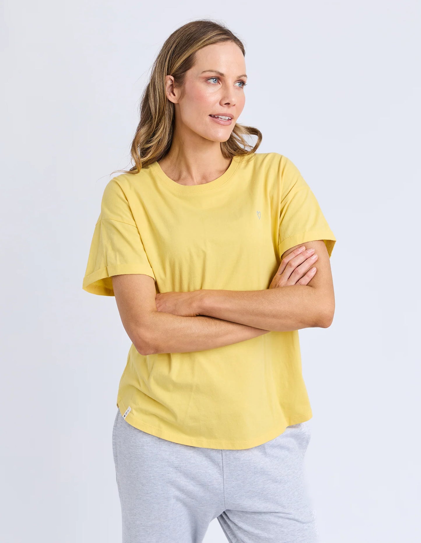 Behind The Trees - Woman wearing a yellow t-shirt with a small logo on a white background - Elm - Halli S/S Tee - Lemon