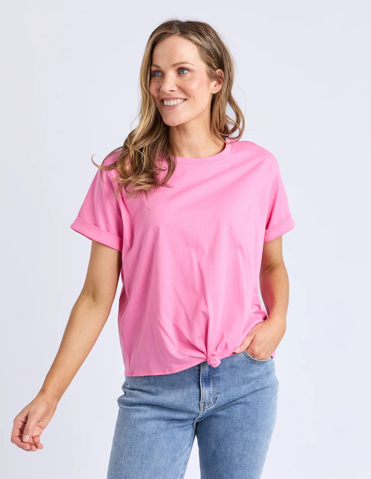 Behind The Trees - Woman wearing a pink t-shirt and denim shorts on a white background - Elm - Knot S/S Tee - Aurora Pink