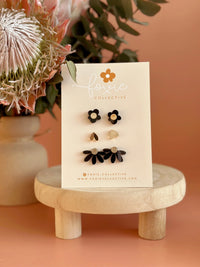 Behind The Trees - Set of floral earrings on a 'Fossil Collective' card with flowers and a wooden stand in the background. - Foxie Collective - Stud Pack trio - Black & Gold