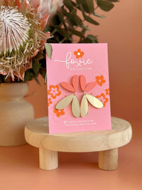 Behind The Trees - Pink card with floral earrings on a wooden stand against a peach background - Foxie Collective - The Love Bug - Pastel Raspberry & Gold