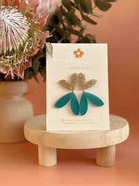 Behind The Trees - Teal and gold earrings on a card with a floral background - Foxie Collective - The Love Bug - Frosted Teal & Gold Glitter