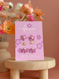 Behind The Trees - Pink card with floral earrings on a wooden stool against a peach background - Foxie Collective - Stud Pack trio - Lilac & Gold