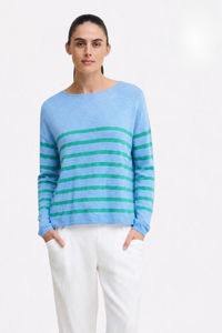 Behind The Trees - A woman modeling a light blue knit sweater with horizontal teal stripes across the chest and sleeves, paired with white trousers, against a plain white studio background. - Little Lies - Bobbie Top - Blue/Jade