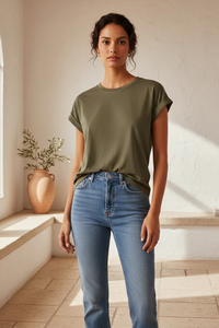 Behind The Trees - Woman wearing an olive green t-shirt and blue jeans standing in a sunlit room. - Little Lies - Rhodes Tee - Khaki
