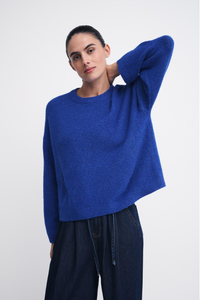 Behind The Trees - A woman modeling a vibrant royal blue knit sweater with a crew neck and long sleeves, paired with dark wide-leg trousers, against a plain light gray background.n - Little Lies - Otto Knit - Cobalt