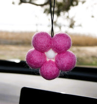 Behind The Trees - Pink felt flower ornament hanging from a car's rearview mirror with a blurred outdoor - Fresh Ballz - Baby Pink Daisy -  Vanilla Bean Fragrancebackground.