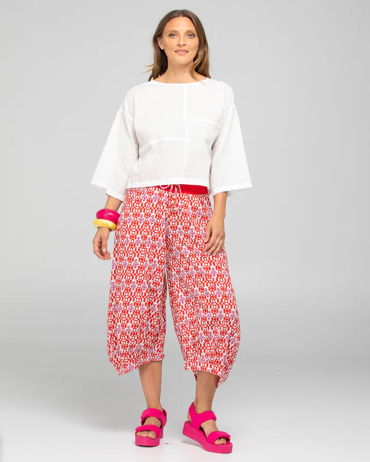Behind The Trees - Woman wearing a white top and red patterned pants on a gray background - Boom Shankar - Guru Pant - Naples Pomodoro 