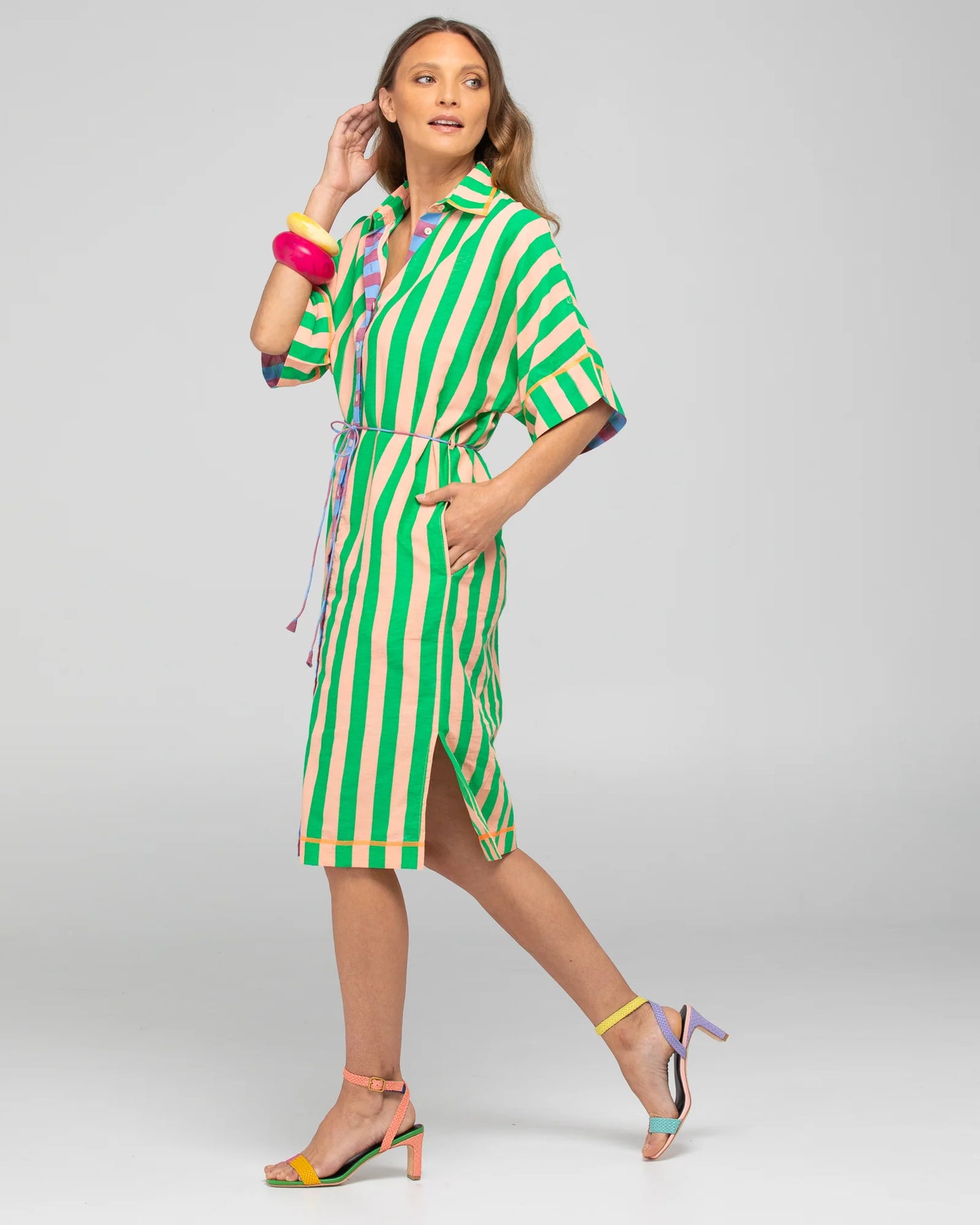 Behind The Trees - Woman wearing a green and white striped dress with colorful accents on a gray background - Boom Shankar - Maui Shirt Dress - Capri Peach