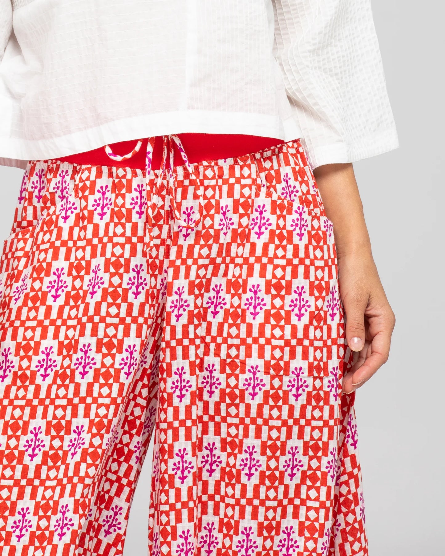 Behind The Trees - Woman wearing a white top and red patterned pants on a gray background - Boom Shankar - Guru Pant - Naples Pomodoro 