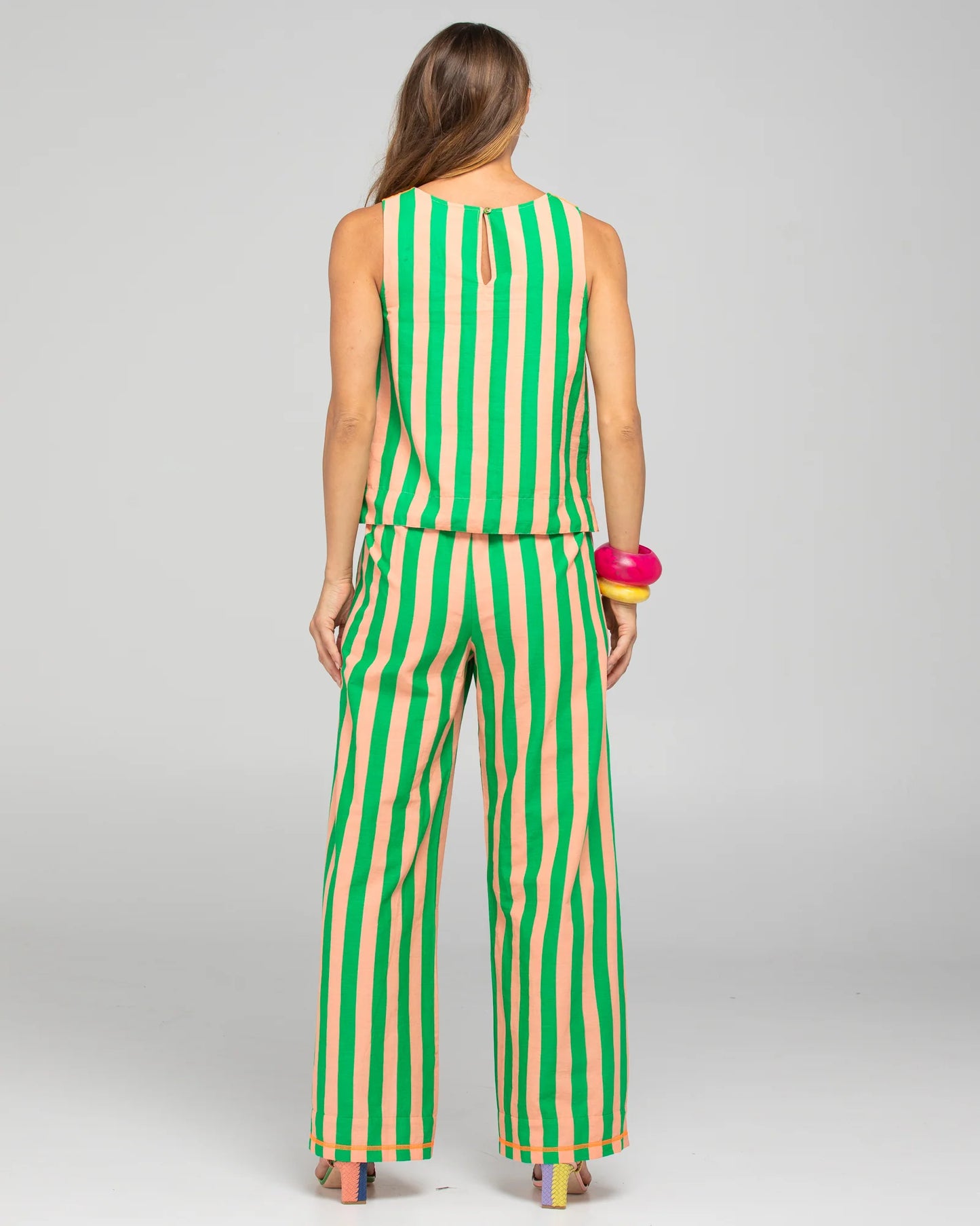 Behind The Trees - Woman wearing a green and beige striped sleeveless top and pants on a gray background - Boom Shankar - Hara Top Reversible - Capri Peach/Tangerine