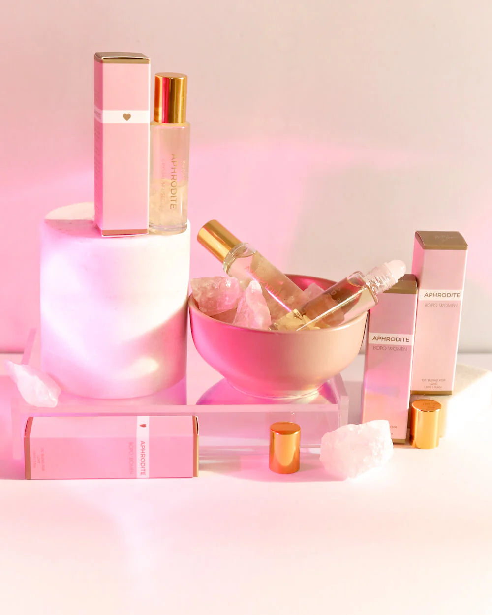 Behind The Trees - A crystal perfume roller with a pink label and clear rollerball bottle, alongside its pink packaging box, displayed on a white marble surface BOPO Women - Crystal Perfume Roller - Aphrodite