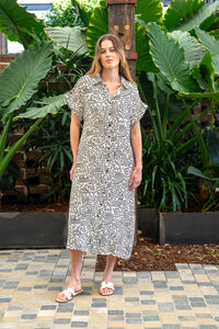 Behind The Trees - Woman in a patterned jumpsuit standing in a garden with large green leaves. - Boho Australia - Elinora Dress - Cream/Black