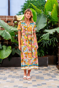 Behind The Trees - Woman wearing a colorful floral dress standing in front of green plants. - Boho Australia - Aamina Midi Dress - Lemon Floral