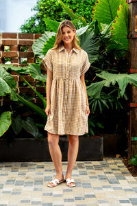 Behind The Trees - Woman in a checkered dress standing in front of large green leaves - Boho Australia - Stephens Dress - Camel Check