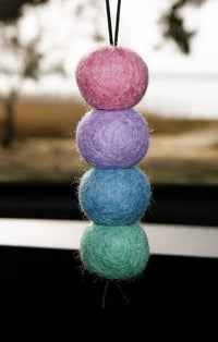 Behind The Trees - A vertical stack of four fuzzy felt balls in pink, purple, blue, and mint green, hanging by a black cord against a blurred outdoor background. - Fresh Ballz - Coral Reef No1 - Fragrance Japanese Honeysuckle - Smelly Balls