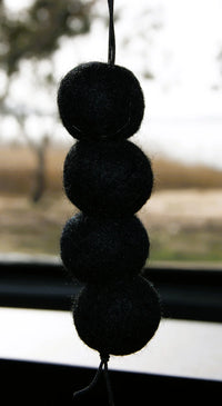 Behind The Trees - Black pom-pom car accessory hanging from a window with a blurred outdoor background - Fresh Ballz - Four BlackZ - Black Ice Type Fragrance - Smelly Balls