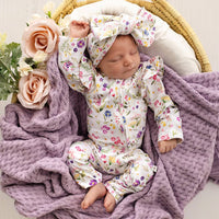 Behind The Trees - A sleeping newborn baby wearing a white long-sleeve floral romper and matching bow headband, posed in a wicker basket with a purple knit blanket and pink roses. - Snuggle Hunny - Organic Snugglesuit Convertible Romper - Gracie