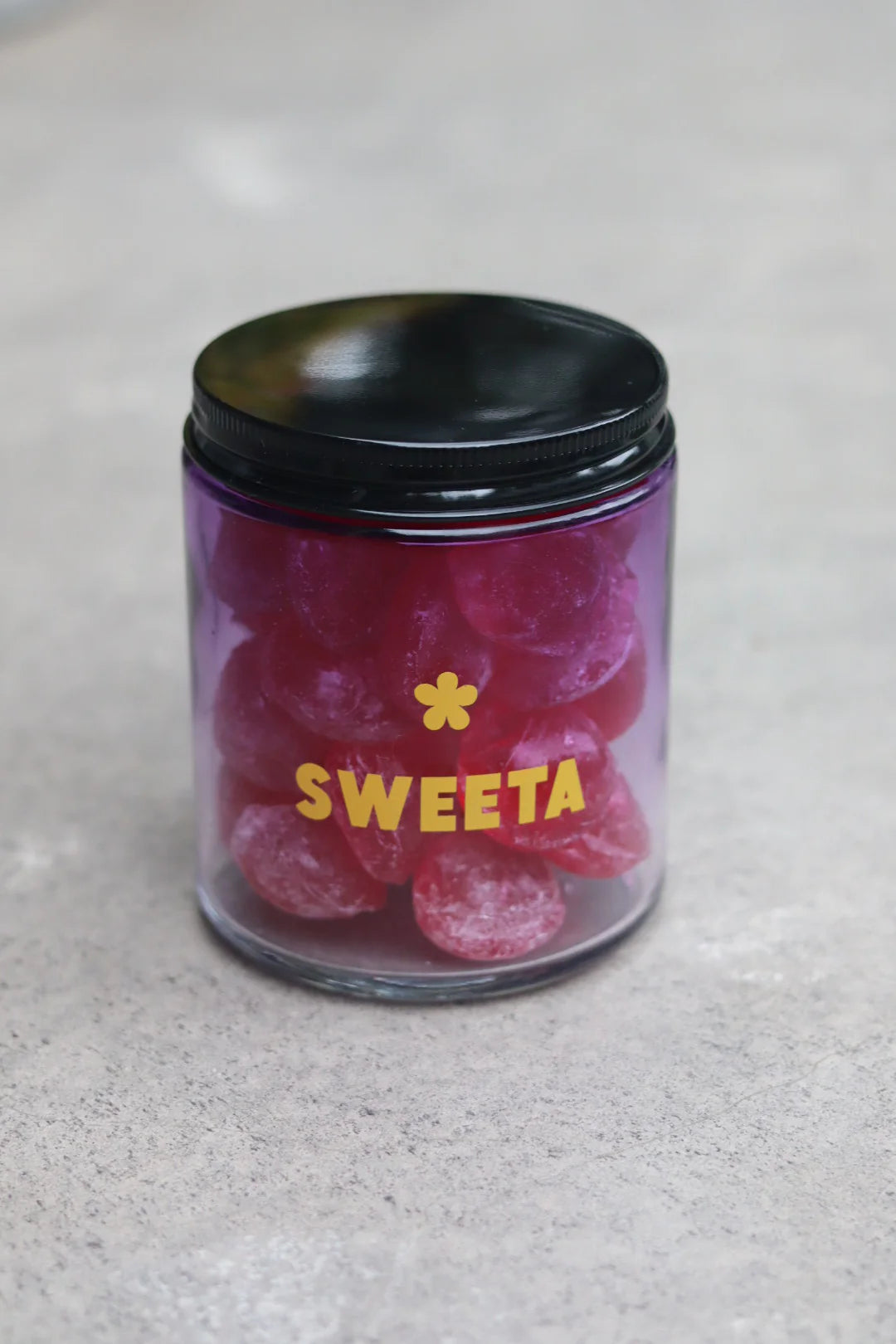 Behind The Trees - Jar of pink gummy bears with a black lid on a gray surface, branded 'SWEETA'. - Sweeta -  Raspberry Drops 180g