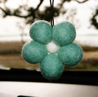 Behind The Trees - Green felt ball car ornament hanging from a car's rearview mirror with a blurred outdoor background. - Fresh Ballz - Mint Green Daisy - Ocean Mist Fragrance - Smelly Balls