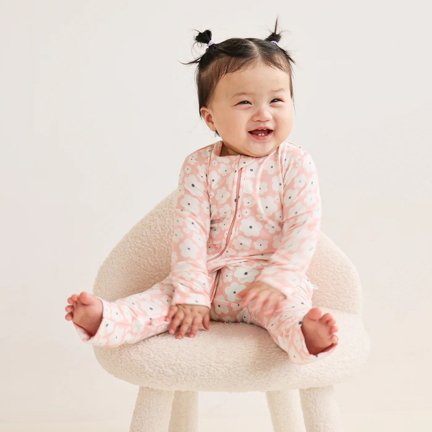 Behind The Trees - KYND Baby - Onesie - Petal Bloom - Baby wearing a pink floral outfit sitting on a white chair. Dandenong Ranges - Emerald - The Lost Woods Market - Baby Shower gift - Baby clothing