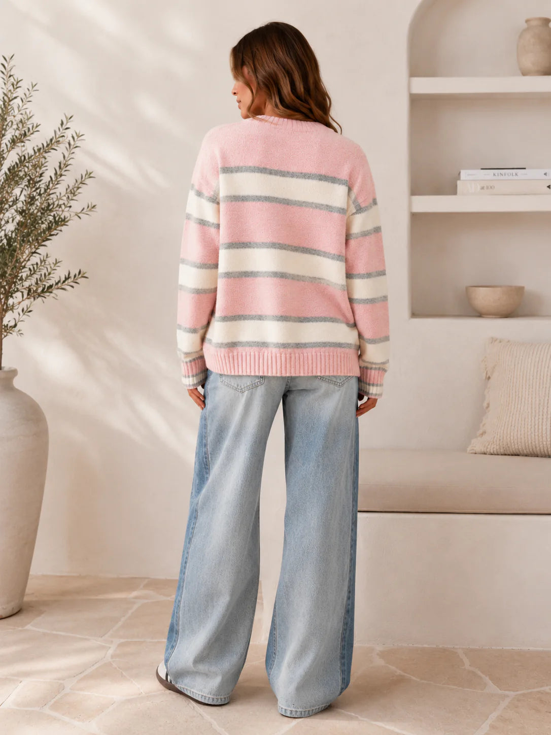 Behind The Trees - Woman wearing a striped sweater and jeans standing in a living room. - Paper Heart - Pina Stripe Knit Jumper - Pink